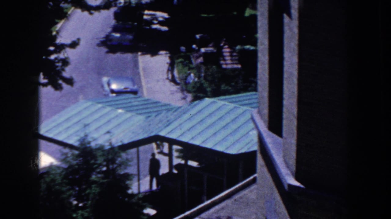 1958 French Lick home-movie frame looking down past a green metal roof toward a street, trees, and a small pedestrian figure.