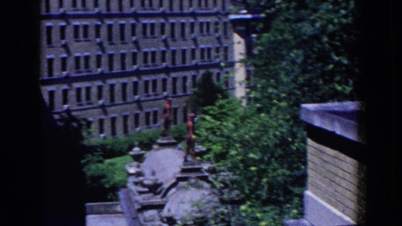Elevated 1958 French Lick view of a brown multi-story building, tree canopy, paths, and a stone ornamental feature.