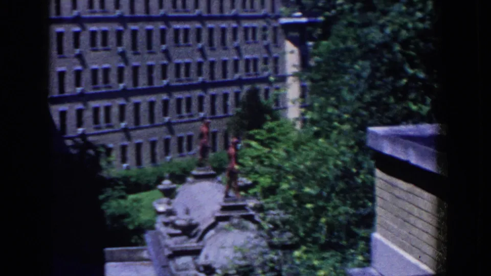 Elevated 1958 French Lick view of a brown multi-story building, tree canopy, paths, and a stone ornamental feature.