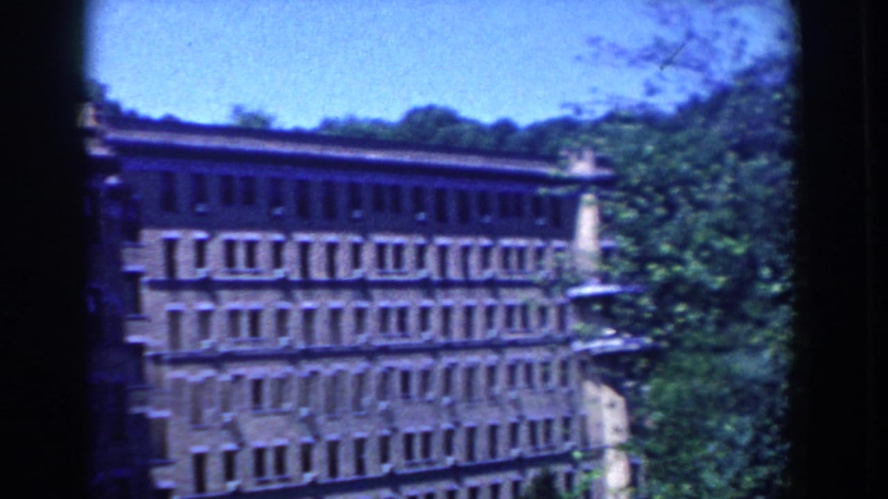1958 French Lick home-movie view of a large brick building with many windows, trees, and bright blue sky.