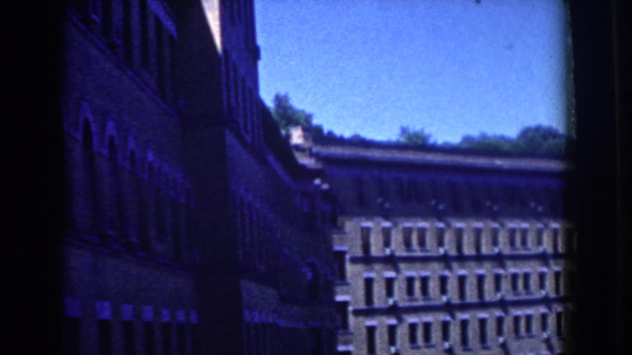 French Lick, Indiana 8mm frame showing a dark brick facade and a second multi-window building in bright daylight.