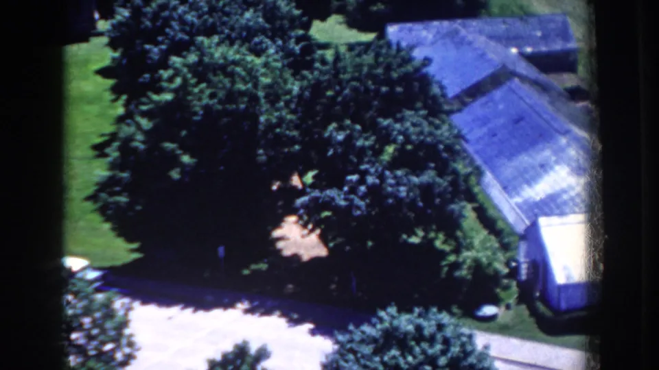1958 8mm frame from French Lick showing a large house roof partly screened by trees, with lawn and driveway below.