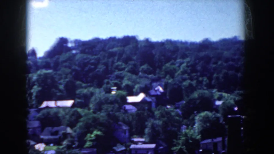 1958 home-movie view across French Lick treetops toward a wooded hillside with scattered roofs below.