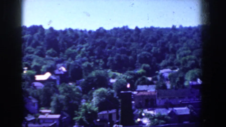 French Lick hillside scene with dense trees, rooftops, and a darker building edge in the foreground.