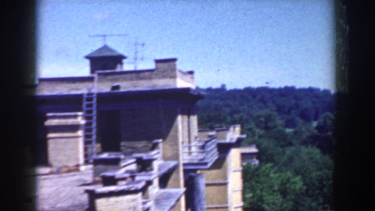 Rooftop edge with a small tower, antennas, trees, and hills beyond.