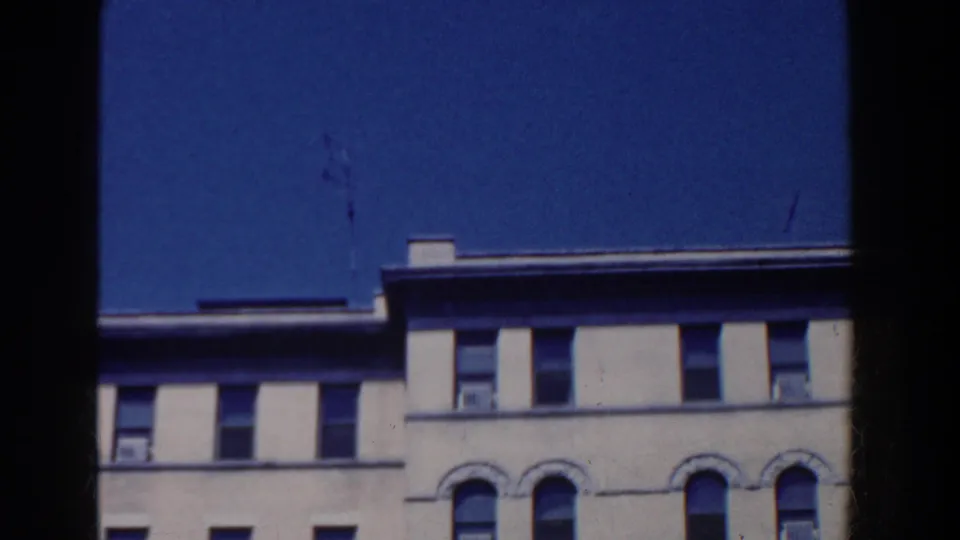 1958 home-movie frame of the building's upper floors in French Lick, with a roofline, arched windows, and visible film grain.
