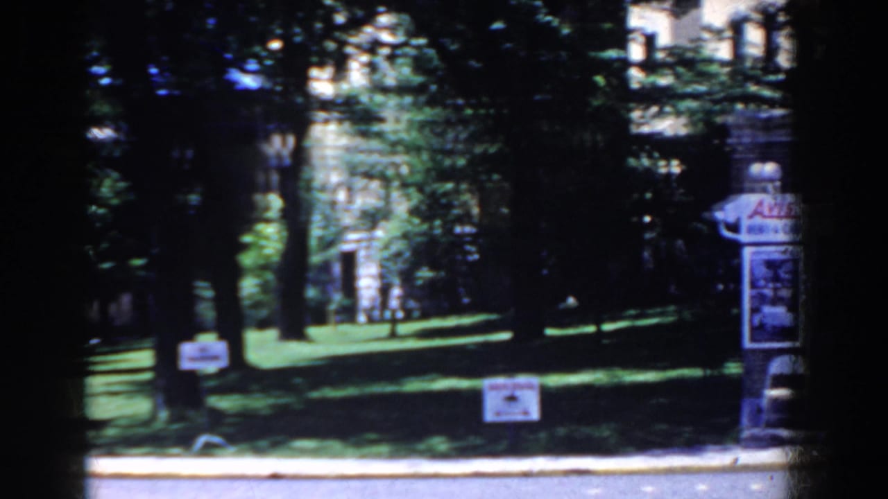 Shaded lawn and trees with a signpost, globe lamp, and part of a sign structure at right.