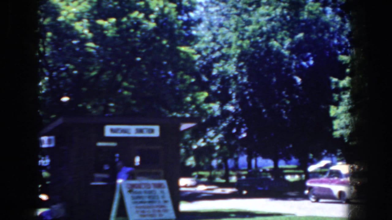 Small park booth under trees with a conducted-tours sign and parked car nearby.