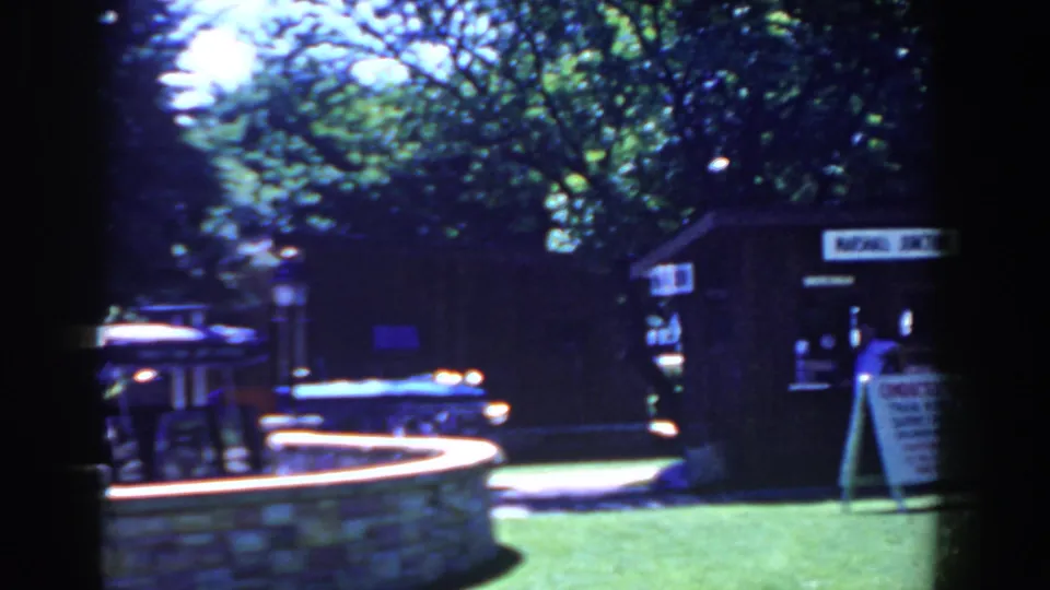 French Lick park scene with stone fountain, lamppost, trees, lawn, and a tour booth in 1958 8mm footage.