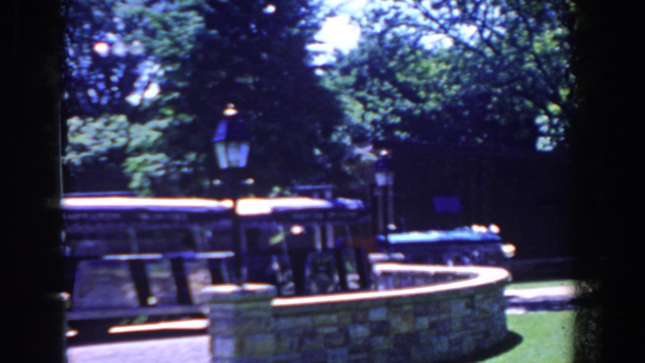 Parked open-sided tour bus behind a stone wall with lampposts and trees.