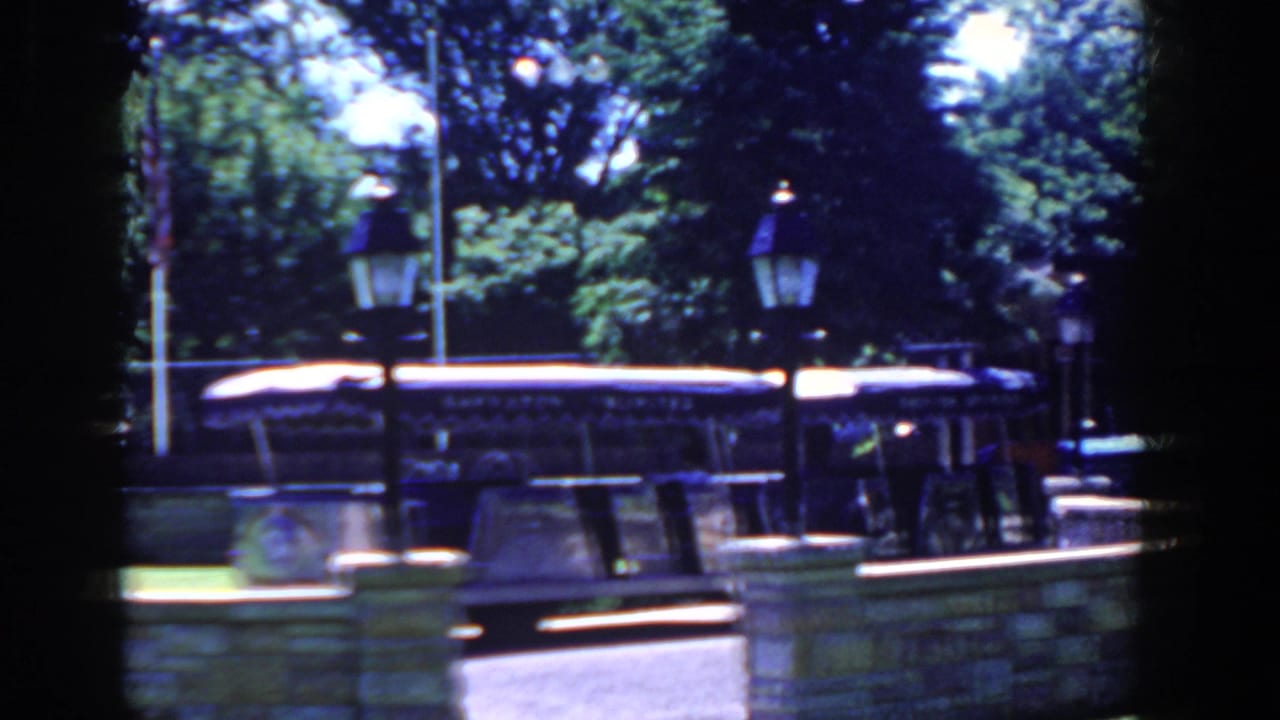 Tour bus beside a stone wall with lampposts, trees, and flagpole behind it.