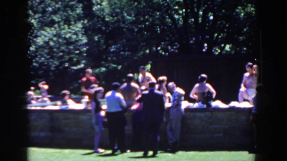 Adults in casual clothing and swimwear gather in bright sun near a low stone pool edge in French Lick, Indiana, 1958.