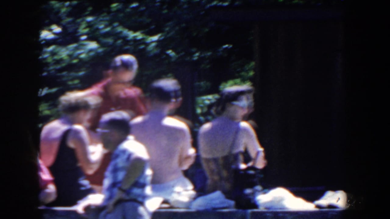 Soft handheld 8mm frame of adults in swimwear and summer clothing by a stone pool edge in French Lick, Indiana.
