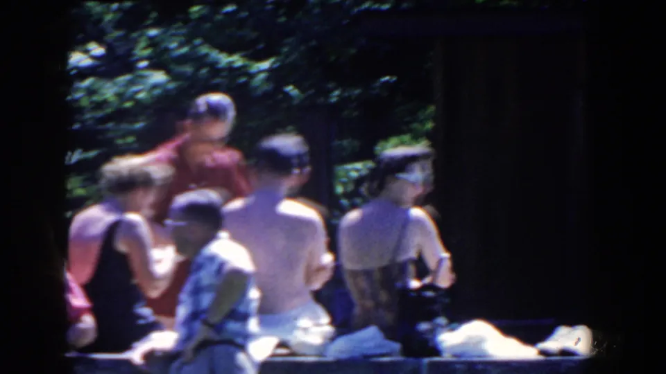 Soft handheld 8mm frame of adults in swimwear and summer clothing by a stone pool edge in French Lick, Indiana.