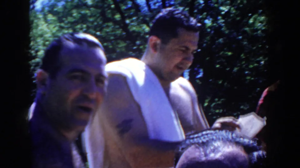 Two men appear in close poolside view as the towel-draped man looks down during a casual 1958 home-movie moment.