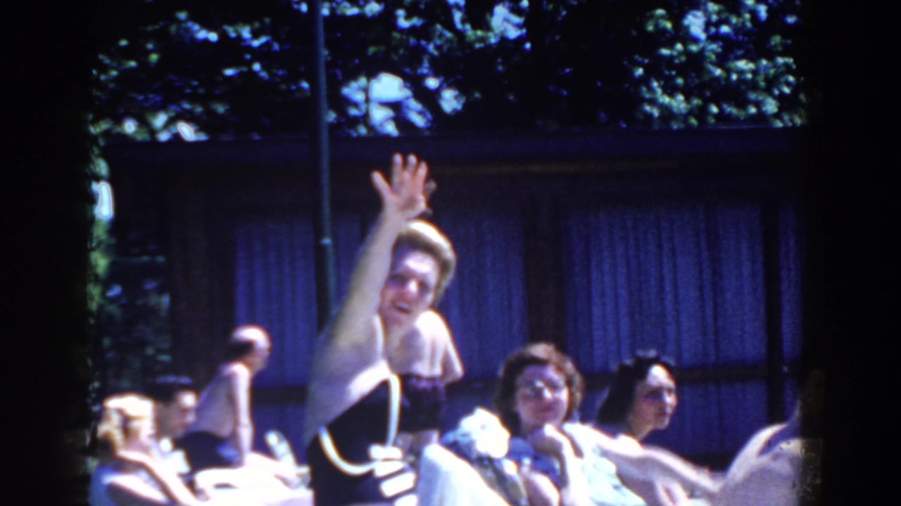 In 1958 French Lick, Indiana footage, a woman waves toward the camera while adults lounge beside a sunny pool area.