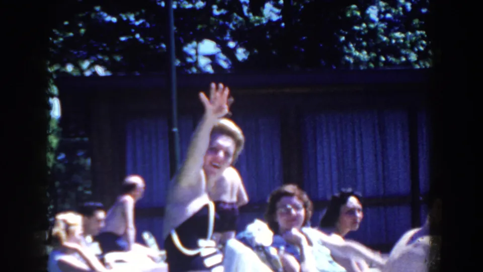In 1958 French Lick, Indiana footage, a woman waves toward the camera while adults lounge beside a sunny pool area.