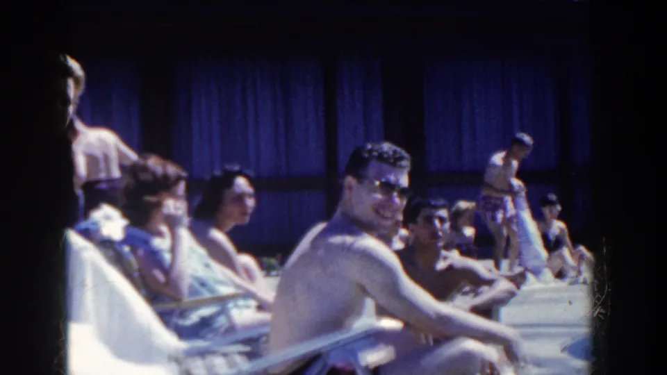 A man in sunglasses sits near the pool edge as other adults sunbathe and converse in 1958 French Lick home-movie footage.