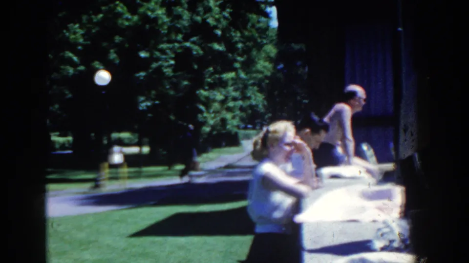 A sunny 1958 French Lick poolside view shows several resort visitors seated along the pool edge near lawns, trees, and a path.