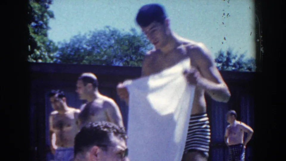 A man dries or unfolds a white towel beside other swimmers at a 1958 French Lick pool gathering.