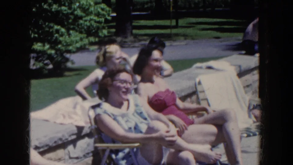 Poolside home-movie frame showing women smiling and relaxing on lounge chairs during a 1958 French Lick gathering.