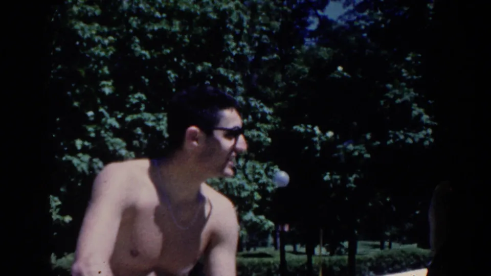 In 1958 French Lick, Indiana, a shirtless man in sunglasses turns near trees during an outdoor resort gathering.