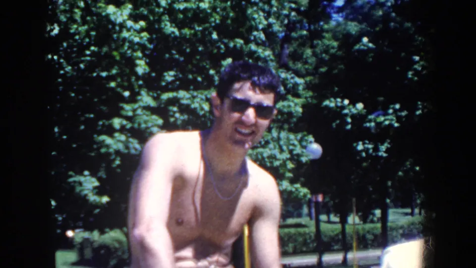 The same shirtless man smiles or speaks toward the camera during the 1958 outdoor resort scene.