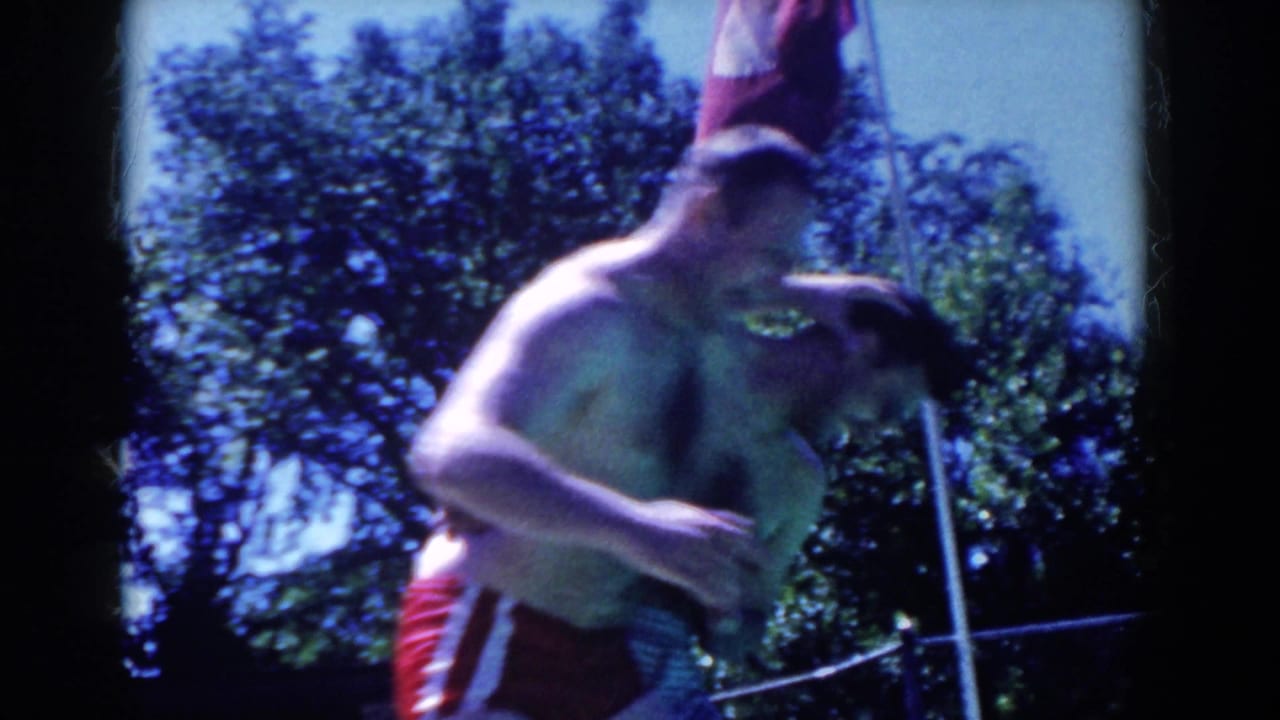 In 1958 French Lick home-movie footage, a shirtless man in red trunks pushes another man near a fenced outdoor pool.