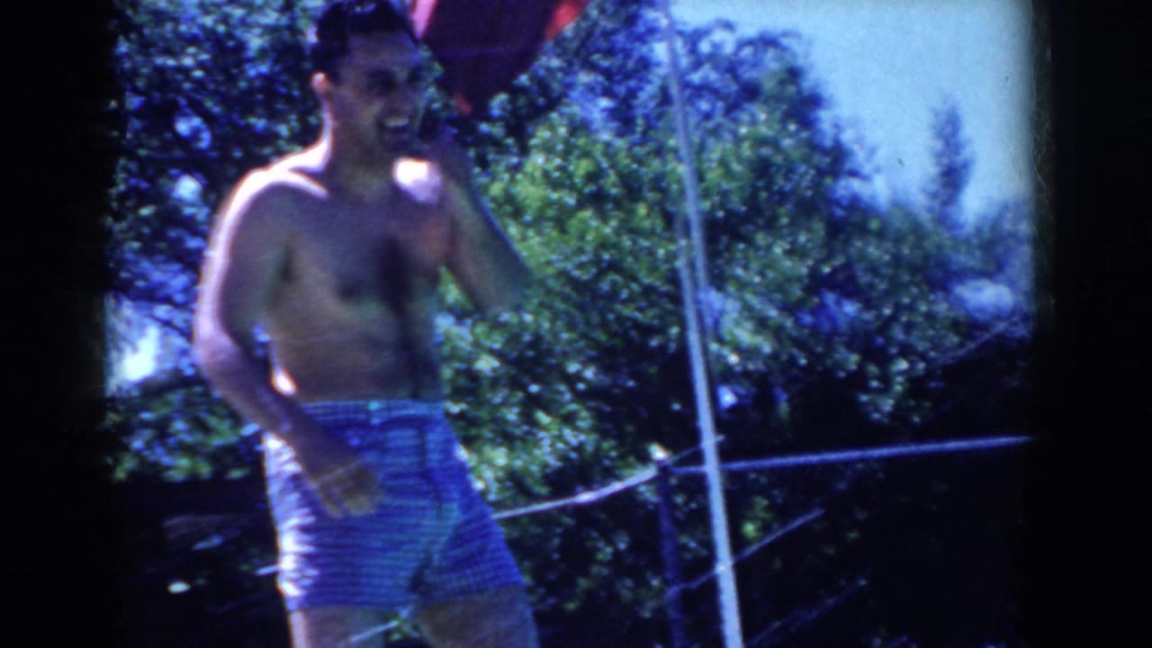 Shirtless man in striped swim trunks standing near the fenced pool area.