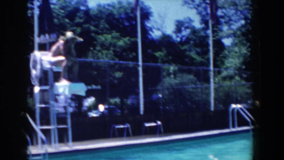 A wide French Lick pool scene shows a seated figure near a high chair, turquoise water, fence, trees, and poolside furniture.