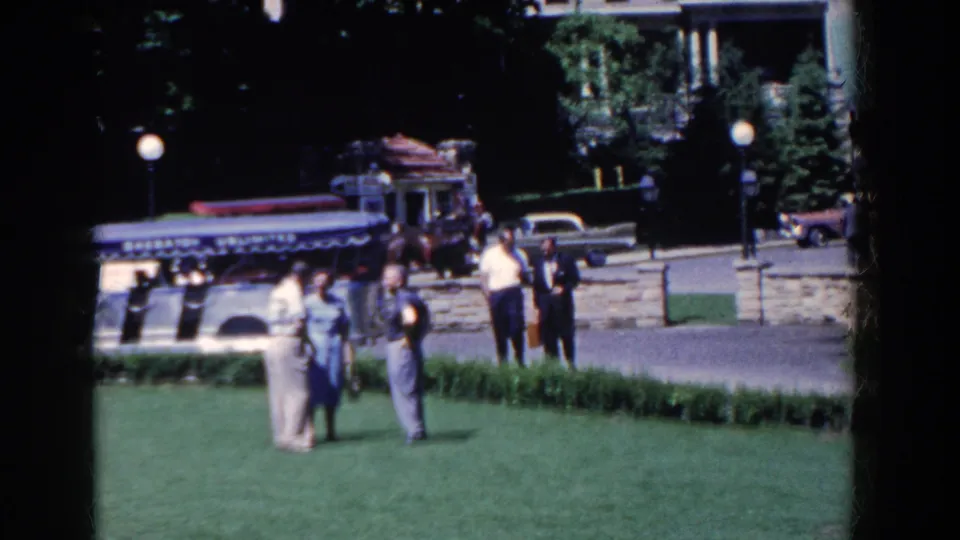 In French Lick, Indiana, adults in 1950s clothing talk on a manicured lawn as classic cars and a horse-drawn carriage pass behind them.