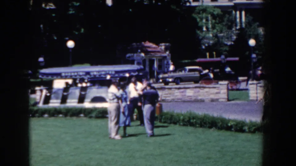 The final frame shows the lawn gathering from a distance, with French Lick street details, classic cars, lamps, and a building beyond the wall.
