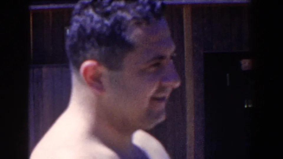 1958 French Lick frame showing a shirtless man smiling in profile near a dark wooden doorway.