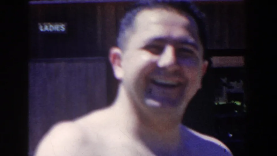 In 1958 French Lick, Indiana home-movie footage, a shirtless adult man smiles toward the camera near a LADIES restroom sign.