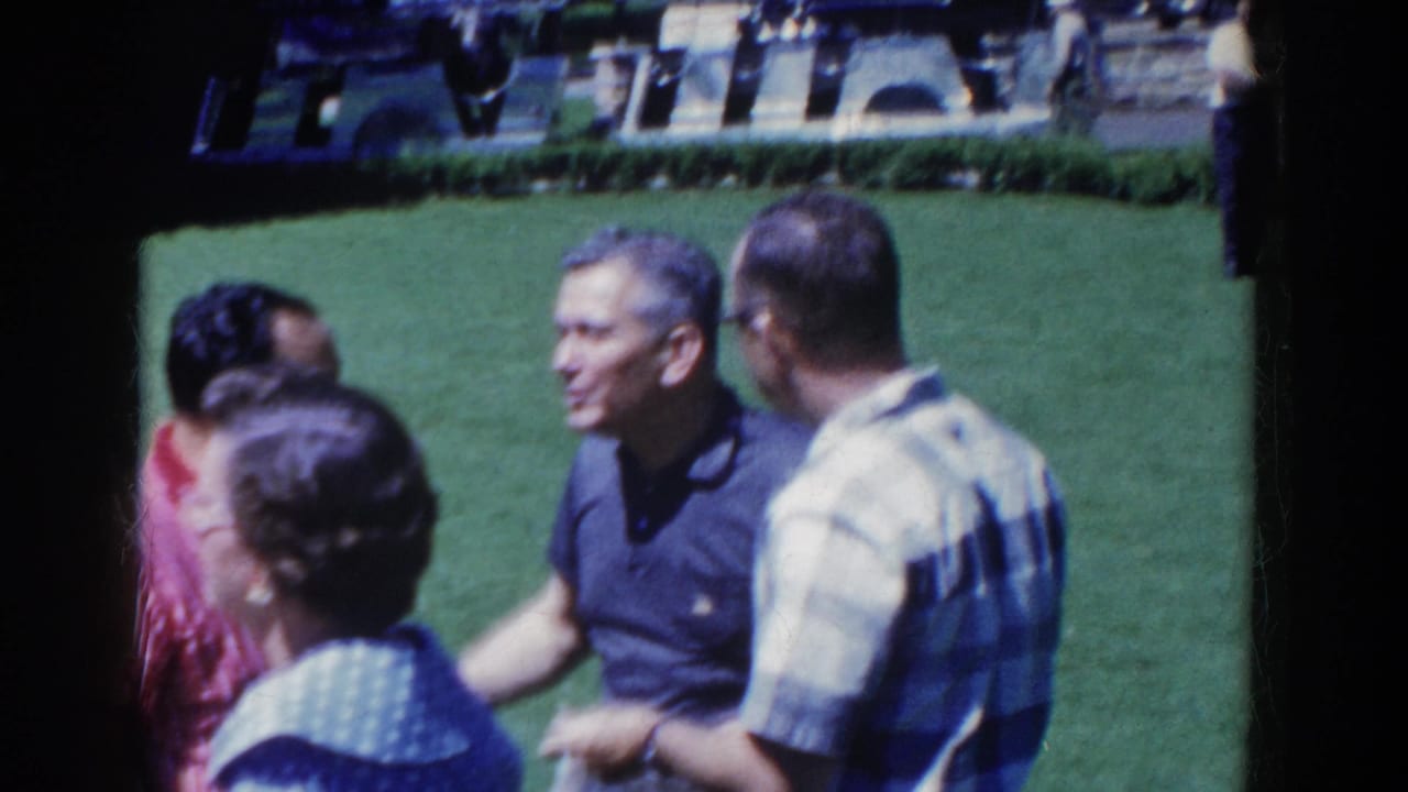 1958 French Lick home-movie frame of adults standing together on a green lawn, with one man smiling during conversation.