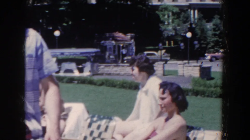 Adults relax and walk on the landscaped grounds near the French Lick hotel, with 1950s clothing and cars visible behind them.