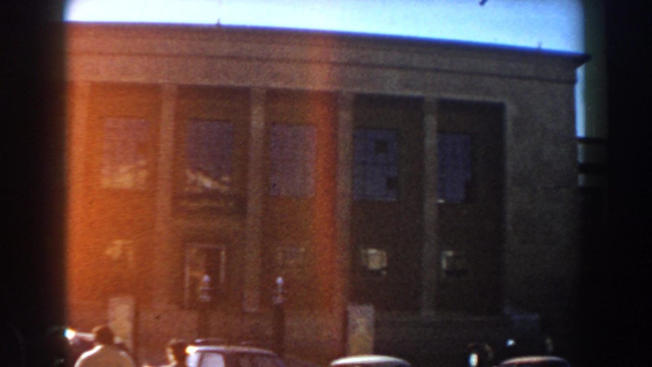 1959 Casablanca street view with a brick multi-story building, parked mid-century cars, and distant pedestrians.
