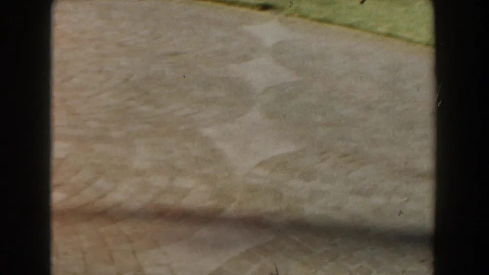 A shifted 8mm frame shows mostly paved ground, with a strip of grass and the street edge barely visible near the top.