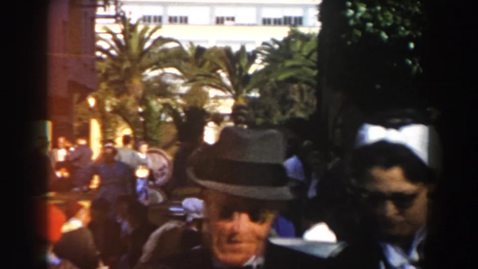 Casablanca 1959 street crowd with a man in a fedora in the foreground, pedestrians behind him, palms, and warm 8mm color flare.