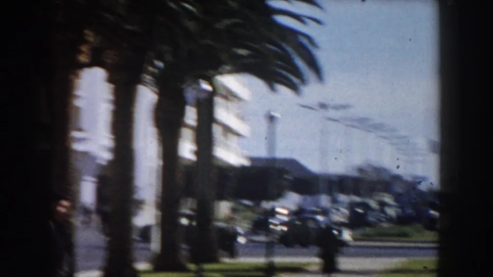 A palm-lined Casablanca boulevard appears in soft 8mm focus, with cars moving or parked near white building fronts.