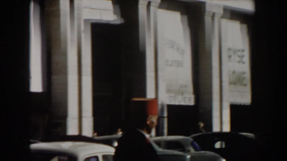 1959 Casablanca street frame showing a man in a red fez beside parked cars and a white building entrance.