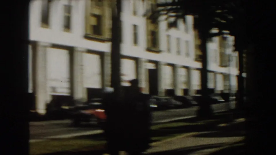 Soft 8mm frame of a Casablanca street with parked cars, palm trunks, and a bright white building facade.