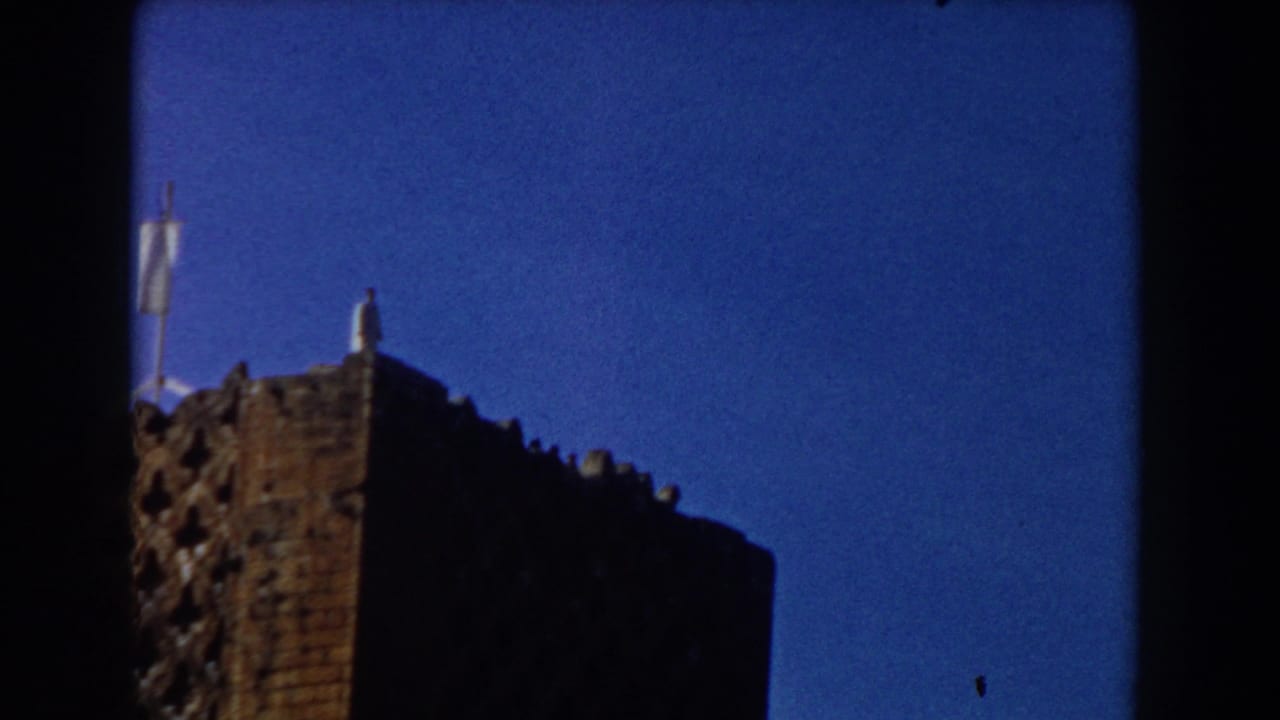 Rooftop corner of a brick building with a distant figure and pale flag or pole.