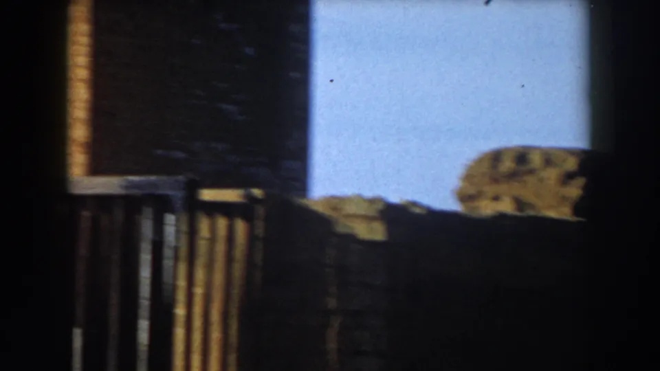 1959 Casablanca 8mm frame looking from shade toward blue sky, railings, low masonry, and a partly obscured stone landmark element.