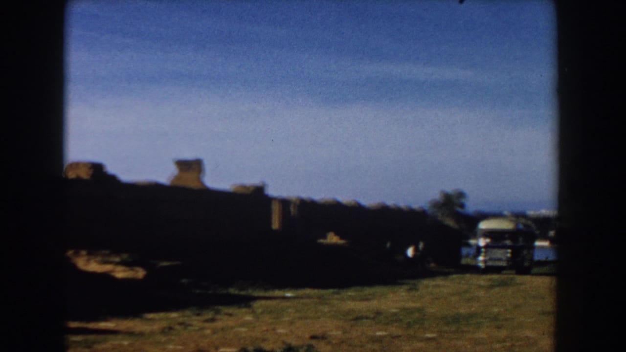 1959 Casablanca travel footage frame with low stone ruins, open ground, and a bus near the right side.