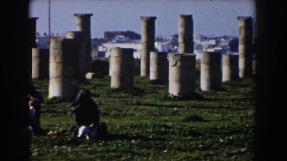 1959 Casablanca home-movie frame showing weathered stone columns in grass with visitors seated among them.