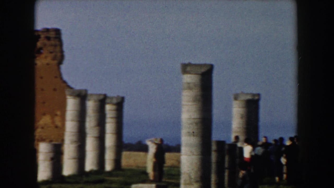 Stone columns and a brick ruin with tourists gathered at the site.