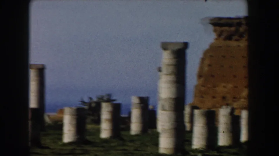 1959 Casablanca home-movie view of columns scattered across grassy ruins with part of a brick structure in the background.