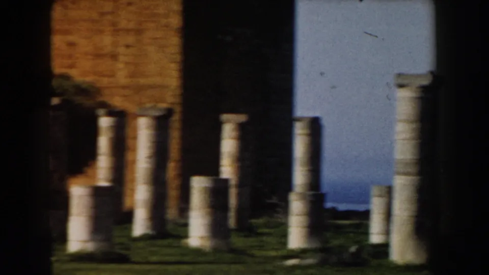 1959 Casablanca-area 8mm frame showing stone columns, broken shafts, grass, a masonry wall, and pale sky at a ruin-like site.