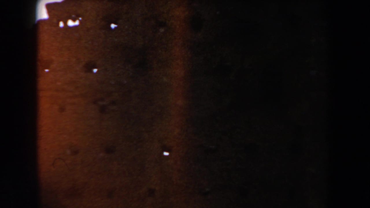 Dark, underexposed view of a reddish masonry wall with film wear and light specks.